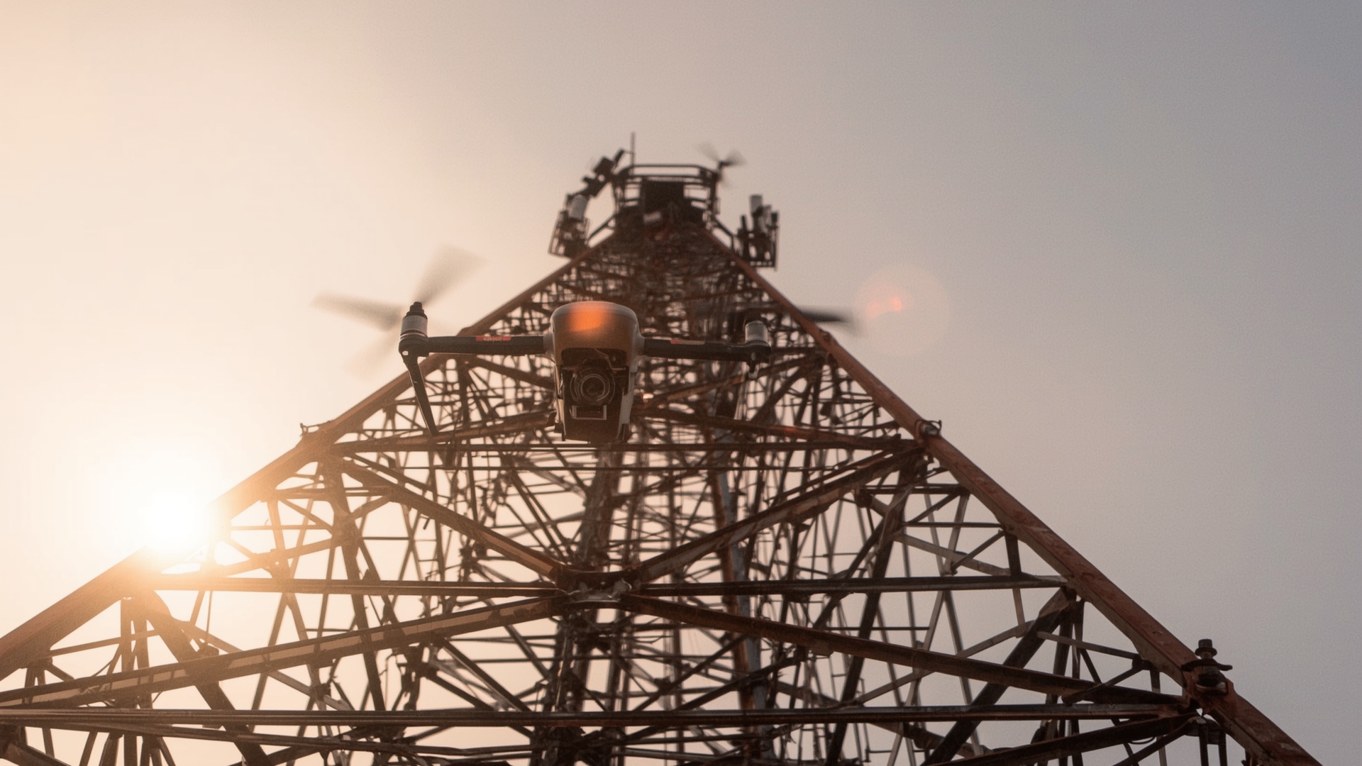 Enterprise inspection drone hovering near cell tower antenna arrays at golden hour
